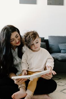 A mother enjoys a cozy reading moment with her young son in the living room.